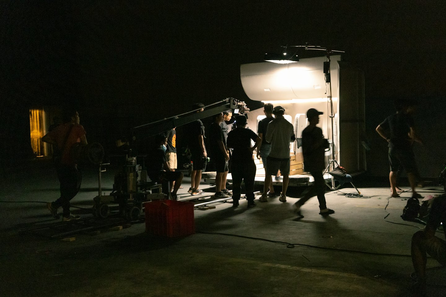 Una troupe cinematografica monta una gru per telecamera in uno studio poco illuminato.
